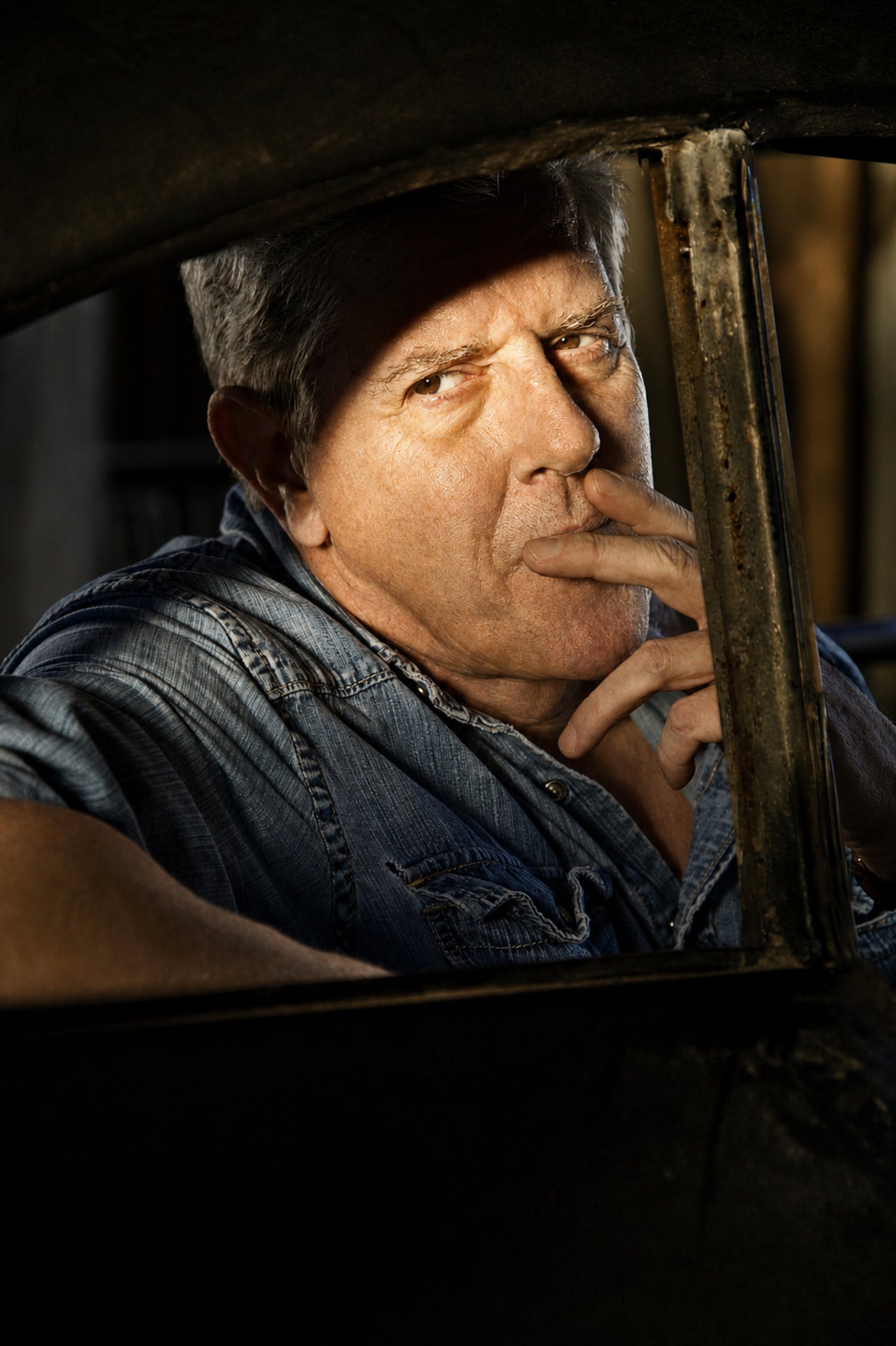 Sam McMurray leaning out of the window of an old truck, lit from the side.